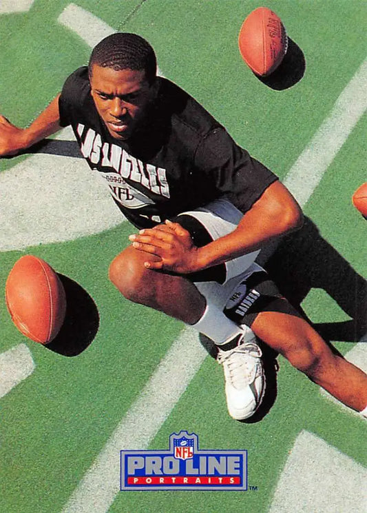 Lionel Washington in black jersey crouching on field surrounded by footballs, Los Angeles Raiders