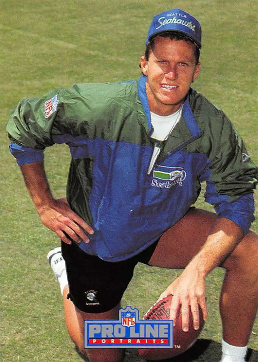 Person in blue and green NFL jacket and cap on grass with Dan McGwire Seattle Seahawks football card