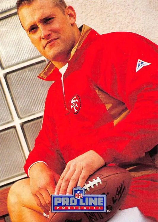 Person in a red NFL Pro Line jacket holding a football, representing Tom Rathman and San Francisco 49ers