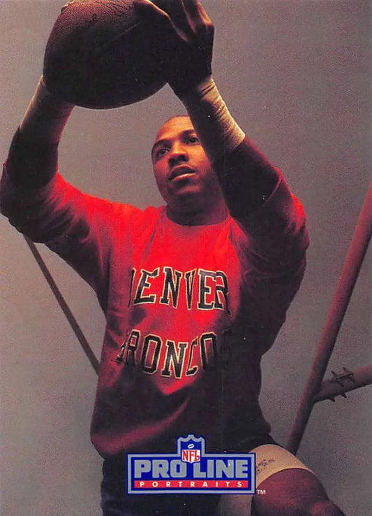 Basketball player in red Denver Broncos sweatshirt holds football above head, Mark Jackson