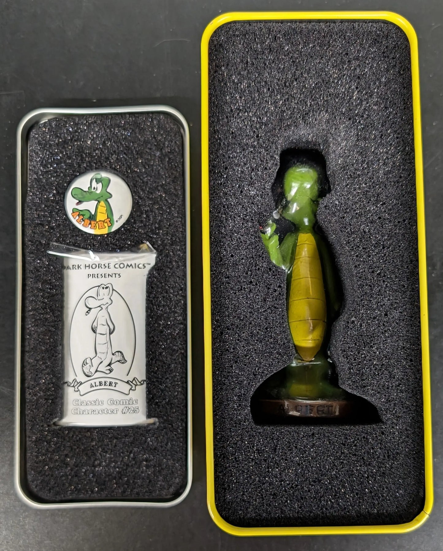 Green and yellow glass bottle-shaped figurine in vintage-style tin box display case