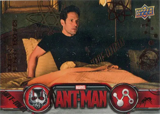 A man sitting on a bed holding a guitar with a Marvel Ant-Man Bronze Base Parallel Chase Card